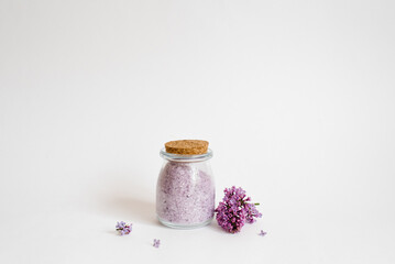 Flavored sea salt with lilac aroma in a glass jar on a light background and flowers. Copy space