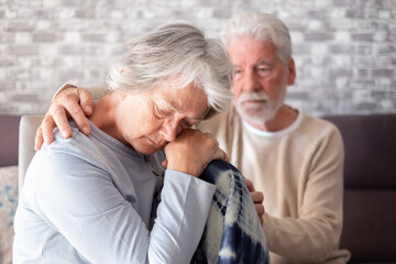 Sad and depressed elderly woman sitting at home while her husband tries to comfort her. Unhappy senior woman needs medical help. Our mind matters