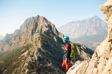 young girl climber in a helmet and with a backpack stands on top of a mountain. mountain climbing