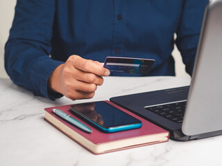 Close-up of hand holding a credit card for shopping online with a laptop while sitting in the office