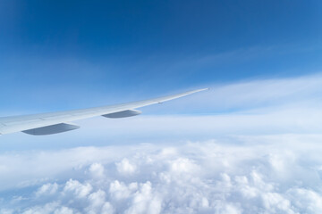 Fototapeta na wymiar Wing of an airplane jet flying above clouds with blue sky from the window in traveling and transportation concept. Nature landscape background.