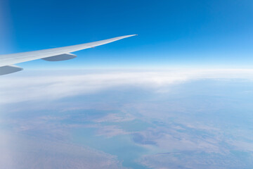 Fototapeta na wymiar Wing of an airplane jet flying above clouds with blue sky from the window in traveling and transportation concept. Nature landscape background.
