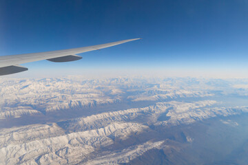 Wing of an airplane jet flying above clouds with blue sky from the window in traveling and transportation concept. Nature landscape background.