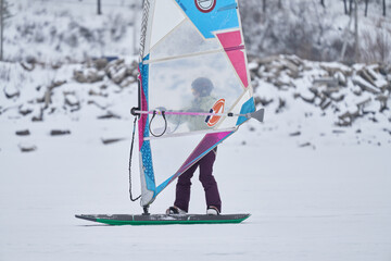A middle-aged woman, a snowsurfer, rides a sailboard. Snowsurfing on a cloudy winter day.