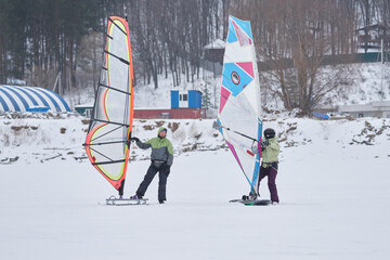 A middle-aged man and woman, snowsurfers, husband and wife, stand, rest and talk. They went snowsurfing on a cloudy winter day.