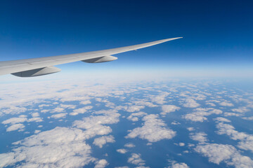 Wing of an airplane jet flying above clouds with blue sky from the window in traveling and transportation concept. Nature landscape background.