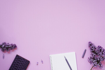 The workspace of a blogger or office worker. Notepad, pen, phone, paper clips, lilac flowers.