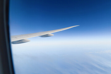 Wing of an airplane jet flying above clouds with blue sky from the window in traveling and transportation concept. Nature landscape background.
