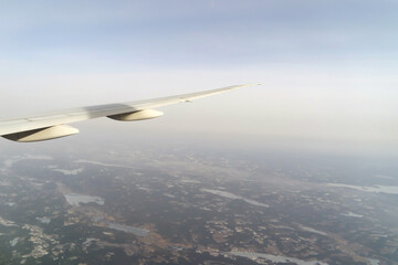 Fototapeta premium Wing of an airplane jet flying above clouds with blue sky from the window in traveling and transportation concept. Nature landscape background.