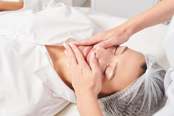 Cosmetologist massages woman face skin after rubbing moisturizing cream for rejuvenation, anti...