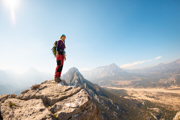 girl climber in a helmet and with a backpack stands on a mountain range against the backdrop of mountains and the sky. mountain climbing