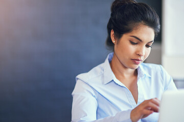 Putting in the hours. Cropped shot of a young businesswoman using her laptop in the office.