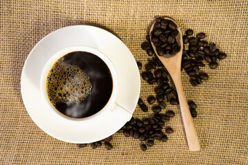 Hot coffee in a white cup of coffee and many coffee beans lying around
