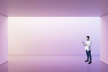 Perspective view on young man using smartphone in empty spacious area with purple shadows wall...