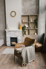 Wicker armchair with a plaid near the fireplace in a country house in the Scandinavian-style living room