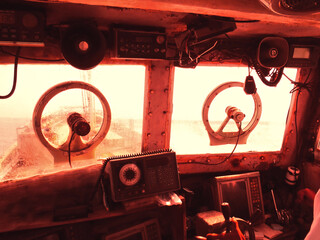 Wheelhouse of an old fishing boat navigating stormy seas. A red image with a sense of danger and fear. © SAIGLOBALNT