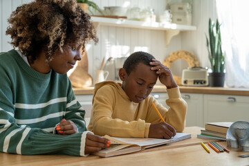 Homeschooling together. Caring African American mother helping thoughtful adopted son with tasks of...
