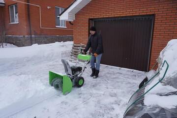 A man cleans snow in the winter in the courtyard of the house,  man cleaning snow with a snow blower
