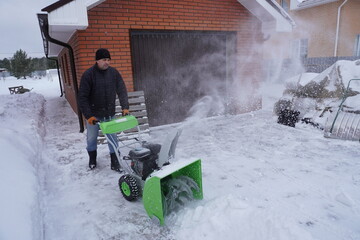 A man cleans snow in the winter in the courtyard of the house,  man cleaning snow with a snow blower