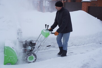 A man cleans snow in the winter in the courtyard of the house,  man cleaning snow with a snow blower