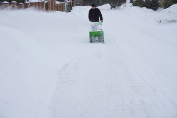 A man cleans snow in the winter in the courtyard of the house,  man cleaning snow with a snow blower
