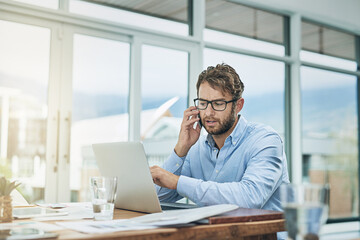 Passion drives his performance. Shot of a young businessman using a phone and laptop at his desk in...