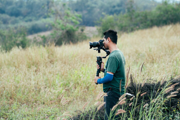 Young Professional videographer holding professional camera on 3-axis gimbal stabilizer. Pro equipment helps to make high quality video without shaking. Cameraman Asian making a videos.