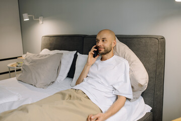 A man is talking on the phone in bed in the bedroom while lying on the bed