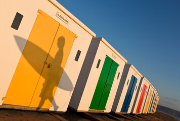 Silhouette of single surfer waling past beach huts Woolacomble ,Devon,UK