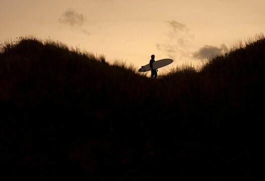 Silhouette of a Lone Surfer among grass looking out to sea, Cornwall ,UK