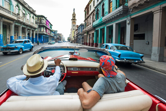 Two Men Driving Convertible Vintage Car In Street Of Havana, Cuba