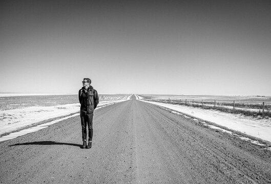 Man stands along long straight flat gravel road in Kansas in winter