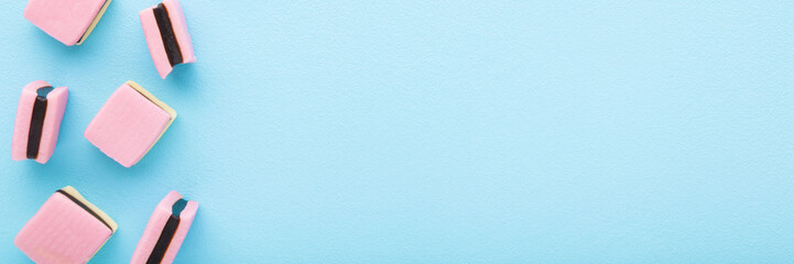 Pink jelly gummy candies with dark chocolate on light blue table background. Pastel color. Sweet snack. Closeup. Empty place for text. Wide banner. Top down view.