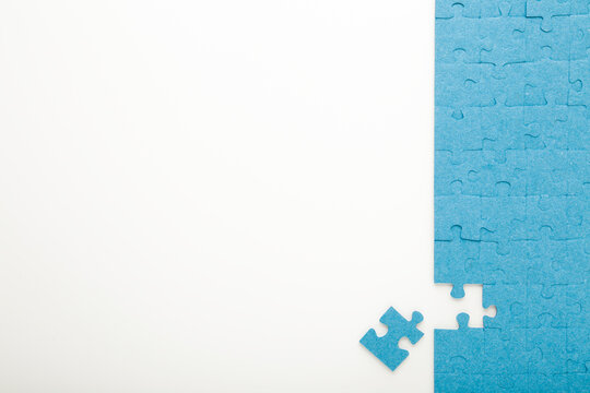 Unfinished blue puzzle with last one piece on white table background. Closeup. Empty place for text. Top down view.