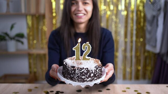 Kids birthday party. Woman mother holding cake with candle number 12. Child turning twelve years old. Decorated home. Family celebrating birthday. Party food. Point of view or POV. Copy space