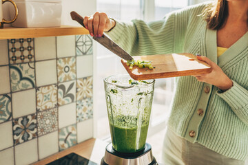 Girl hands prepare a green smoothie, puts fresh spinach leaves in a blender. Healthy eating...