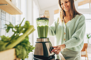 Woman preparing tasty green smoothie in kitchen