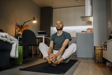 A man in sportswear is engaged in yoga training on a stylish carpet in a modern apartment in his spare time.
