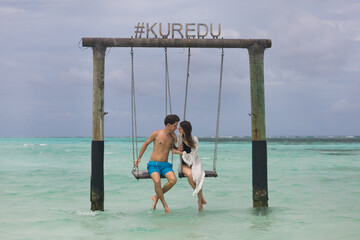 A young couple is swinging on a swing on a tropical beach in the Maldives. Summer holidays