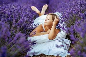 A middle-aged woman lies in a lavender field and enjoys aromatherapy. Aromatherapy concept, lavender oil, photo session in lavender