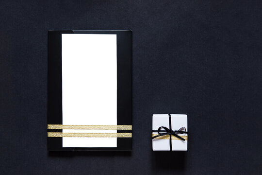 black envelope mockup, shot from the top on a black background with copy space. Tied with a gold ribbon. Gift box with ribbon. white blank card for text. Business invitation, Father's Day.
