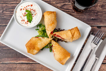Pacanga pastry with salad and yogurt sauce on a white porcelain plate