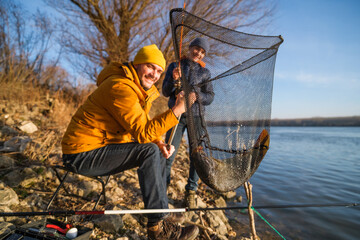 Father and son are fishing on sunny winter day. They caught a fish and are holding it in a landing...