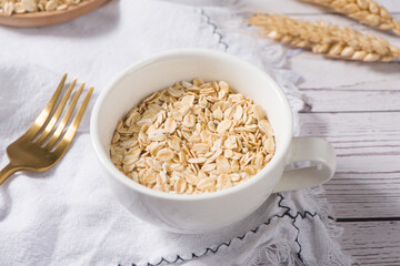 Dry rolled oat flakes oatmeal in cup on wooden table