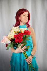 Beautiful woman with red hair in yellow dress on a light background holds a large bouquet of roses flowers. Inernational woman's day 8 March