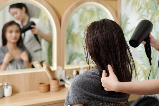 Hairdresser blow drying hair of female client