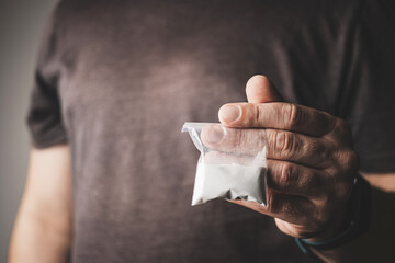 Man's hand holds transparent plastic packet with cocaine powder, drug dealer selling drugs. Drug abuse and addiction concept