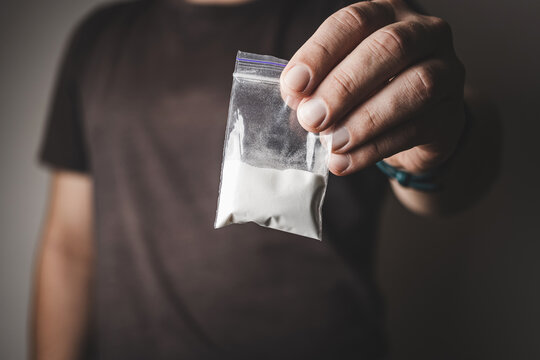 Man's hand holds transparent plastic packet with cocaine powder, drug dealer selling drugs. Drug abuse and addiction concept