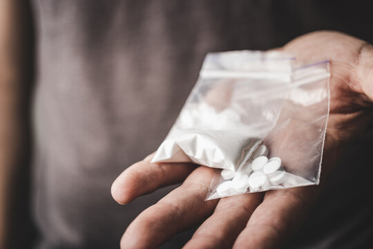 Man's hand holds two transparent plastic packets with cocaine powder and white pills lsd, drug dealer selling drugs. Drug abuse and addiction concept