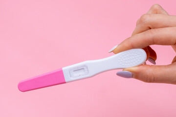 Womans hand holding a pregnancy test on pink background with copy space.